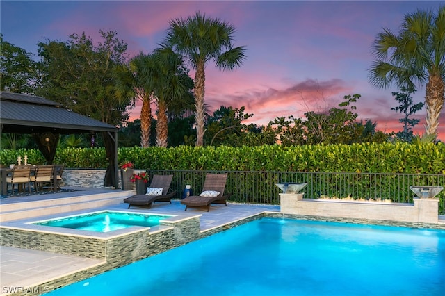 pool at dusk featuring an in ground hot tub, pool water feature, a gazebo, and a patio area