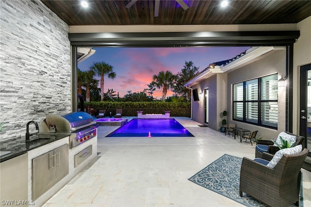 pool at dusk featuring exterior kitchen, a hot tub, grilling area, and a patio area