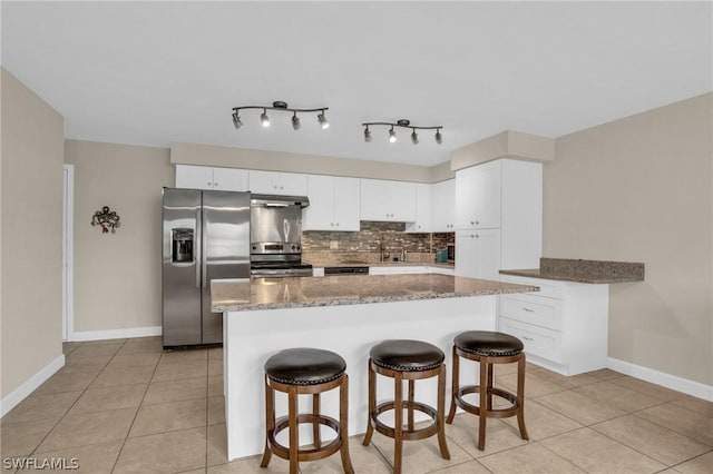 kitchen featuring backsplash, dark stone counters, stainless steel appliances, light tile patterned floors, and white cabinets