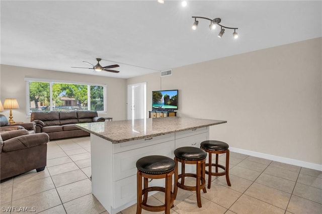 kitchen with light stone countertops, a kitchen bar, a center island, and white cabinetry