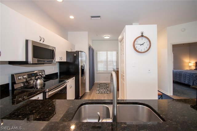 kitchen with dark stone countertops, light carpet, white cabinetry, and appliances with stainless steel finishes