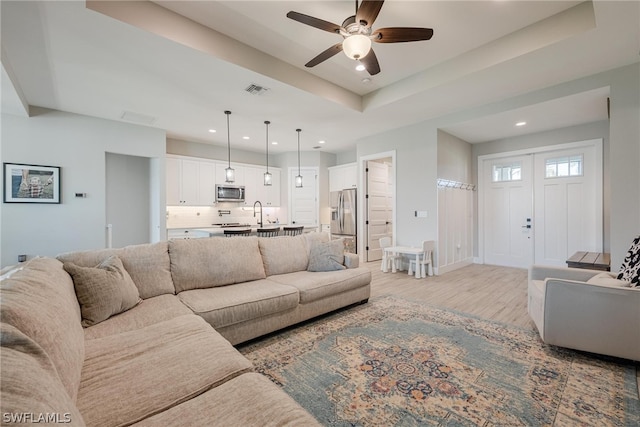 living room featuring a raised ceiling, sink, ceiling fan, and light wood-type flooring