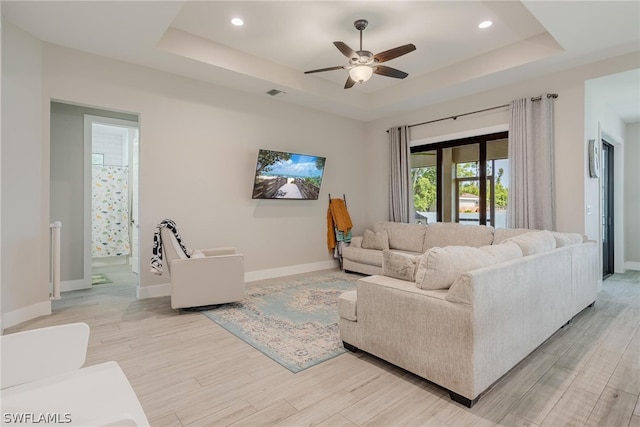 living room featuring light wood-type flooring, a tray ceiling, and ceiling fan