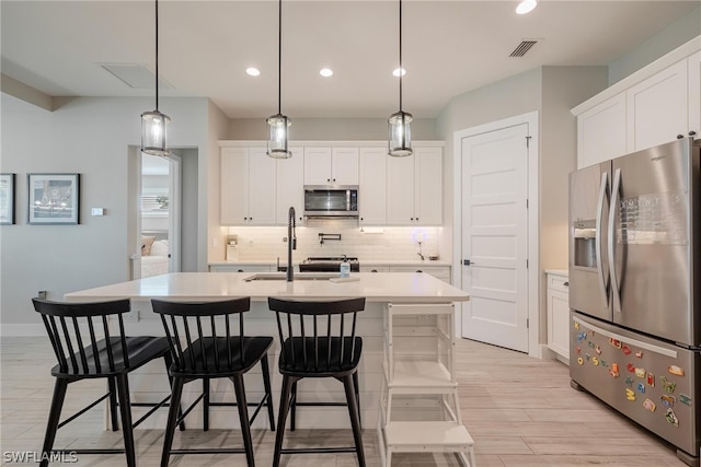 kitchen featuring appliances with stainless steel finishes, an island with sink, white cabinets, decorative light fixtures, and tasteful backsplash