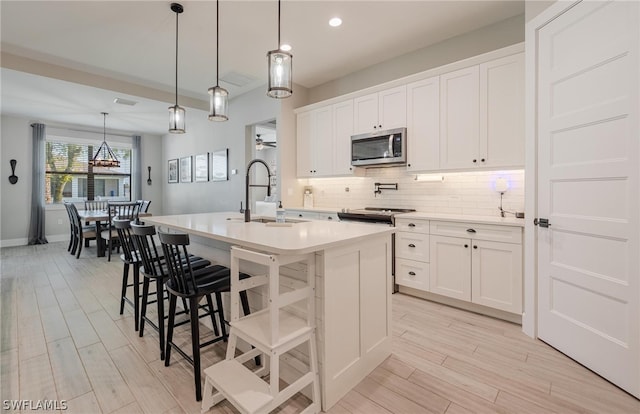 kitchen with backsplash, hanging light fixtures, a breakfast bar area, an island with sink, and white cabinets