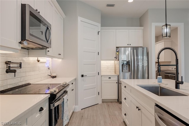 kitchen with light wood-type flooring, appliances with stainless steel finishes, white cabinets, pendant lighting, and tasteful backsplash