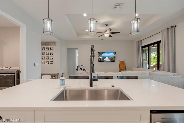 kitchen featuring independent washer and dryer, hanging light fixtures, ceiling fan, a raised ceiling, and sink