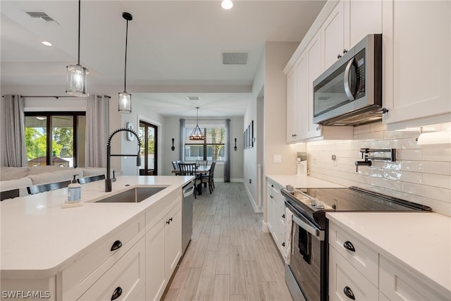 kitchen with appliances with stainless steel finishes, an island with sink, white cabinets, pendant lighting, and sink