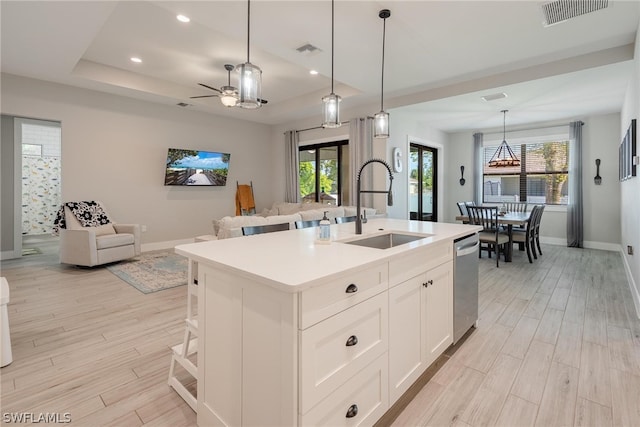 kitchen with light wood-type flooring, an island with sink, decorative light fixtures, sink, and dishwasher