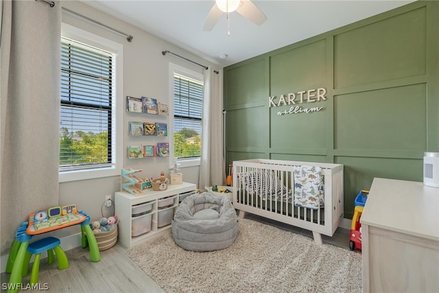 bedroom featuring a nursery area, light hardwood / wood-style flooring, ceiling fan, and multiple windows