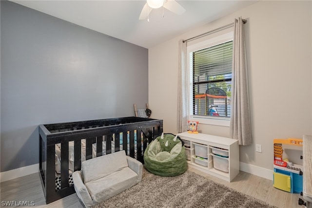 bedroom with hardwood / wood-style flooring, a crib, and ceiling fan