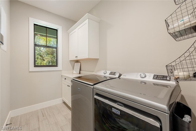 clothes washing area with washer and clothes dryer, cabinets, and light wood-type flooring