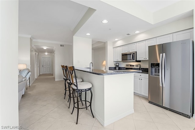 kitchen featuring stainless steel appliances, light tile flooring, ornamental molding, white cabinets, and a breakfast bar area