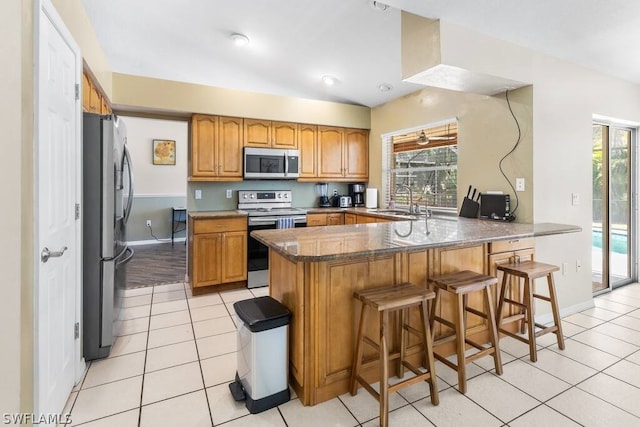 kitchen featuring appliances with stainless steel finishes, kitchen peninsula, a kitchen bar, sink, and light tile floors