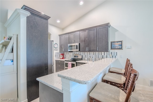 kitchen with kitchen peninsula, tasteful backsplash, stainless steel appliances, light tile floors, and a breakfast bar area