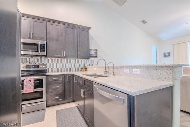 kitchen with vaulted ceiling, light tile flooring, backsplash, sink, and appliances with stainless steel finishes