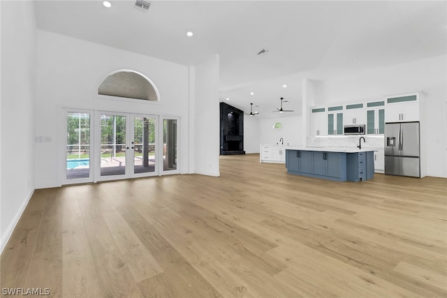 unfurnished living room with french doors, a towering ceiling, and light wood-type flooring