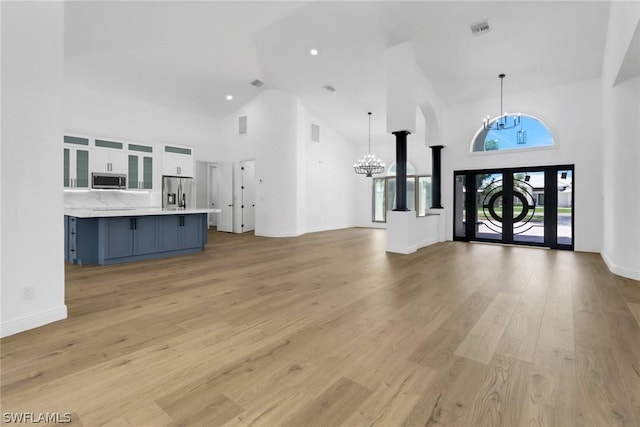 unfurnished living room with high vaulted ceiling, light wood-style flooring, visible vents, and a notable chandelier