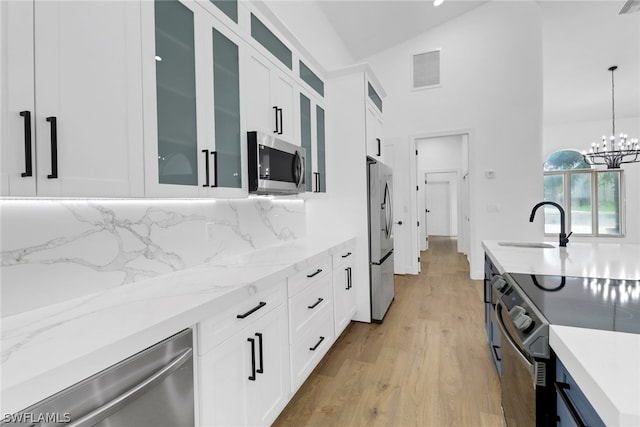 kitchen with appliances with stainless steel finishes, hanging light fixtures, light hardwood / wood-style floors, white cabinets, and decorative backsplash