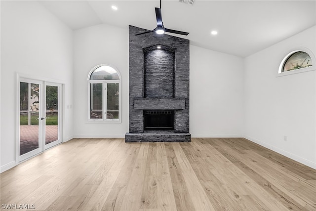 unfurnished living room featuring ceiling fan, a stone fireplace, high vaulted ceiling, and light hardwood / wood-style floors