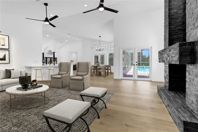 living room with high vaulted ceiling, a stone fireplace, light hardwood / wood-style floors, and ceiling fan