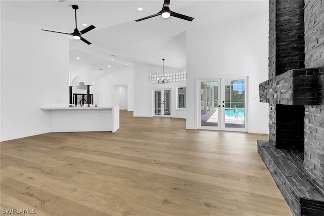 unfurnished living room with a stone fireplace, french doors, ceiling fan, and light wood-type flooring