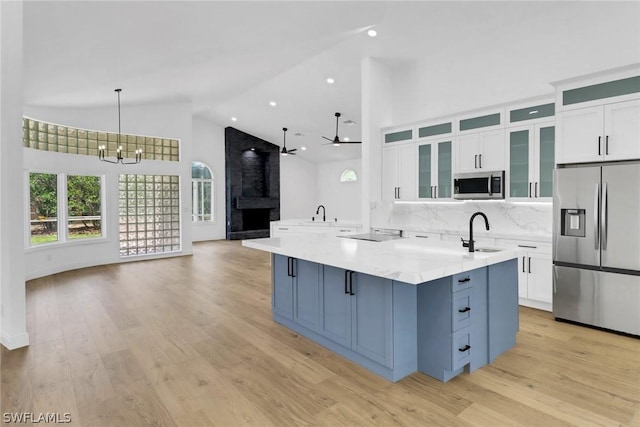 kitchen with stainless steel appliances, ceiling fan with notable chandelier, a sink, light wood finished floors, and white cabinets