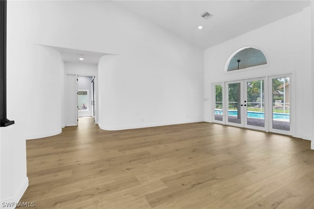 unfurnished living room with light wood-type flooring, high vaulted ceiling, and french doors