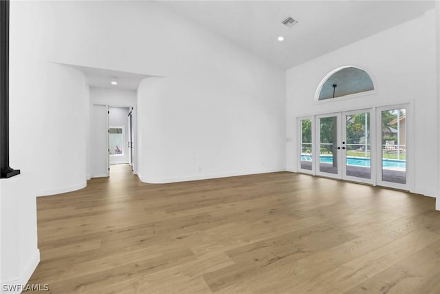 unfurnished room featuring baseboards, high vaulted ceiling, wood finished floors, and french doors