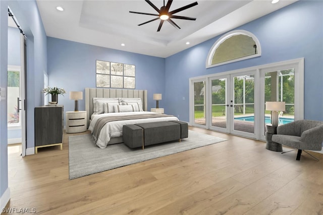 bedroom featuring french doors, a barn door, a raised ceiling, access to exterior, and light hardwood / wood-style floors