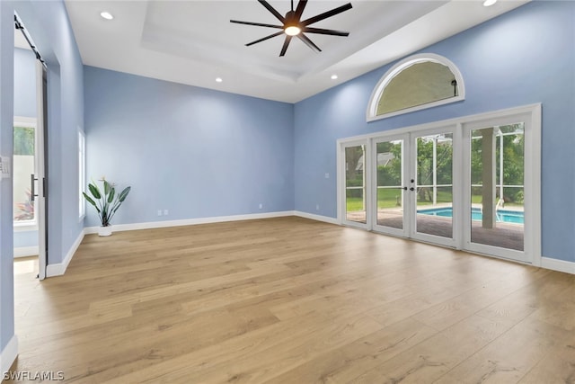 spare room featuring french doors, light hardwood / wood-style flooring, a tray ceiling, ceiling fan, and a barn door