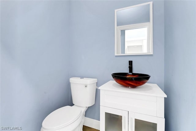 half bath with baseboards, toilet, and vanity