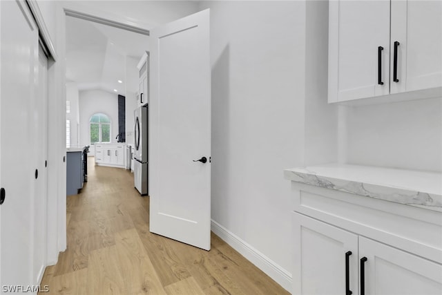 corridor with baseboards, lofted ceiling, and light wood-style flooring