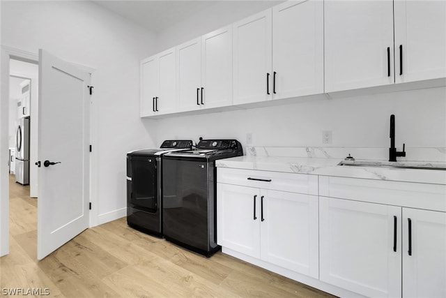 laundry area featuring baseboards, washing machine and clothes dryer, a sink, light wood-style floors, and cabinet space