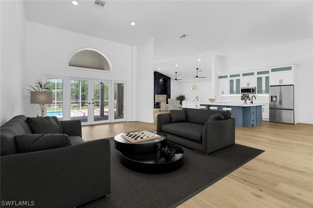 living room with recessed lighting, french doors, a towering ceiling, light wood-style floors, and visible vents