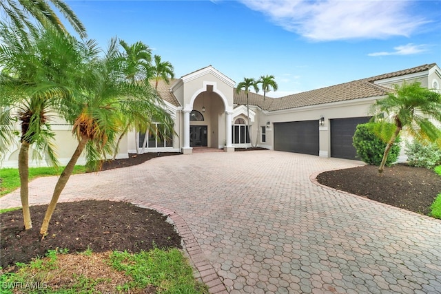 mediterranean / spanish home featuring a tiled roof, decorative driveway, an attached garage, and stucco siding