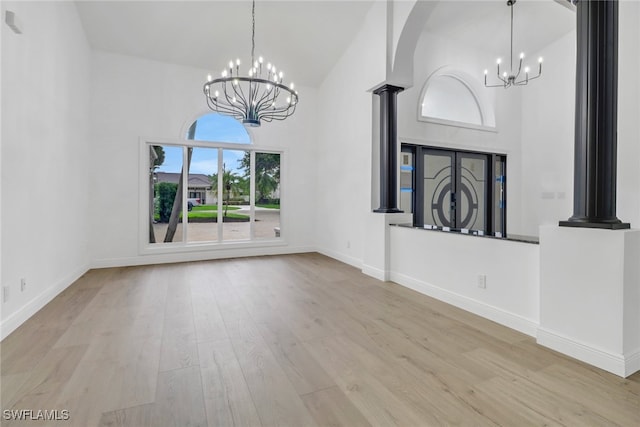 unfurnished living room with decorative columns, wood finished floors, baseboards, a towering ceiling, and an inviting chandelier