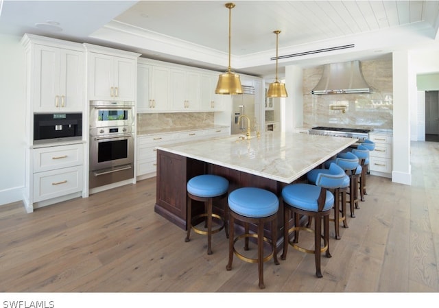 kitchen featuring hardwood / wood-style floors, stainless steel double oven, backsplash, wall chimney range hood, and white cabinets