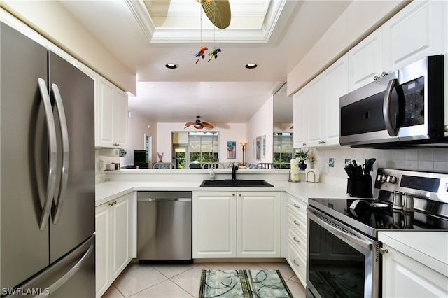 kitchen with white cabinets, stainless steel appliances, ceiling fan, a tray ceiling, and sink