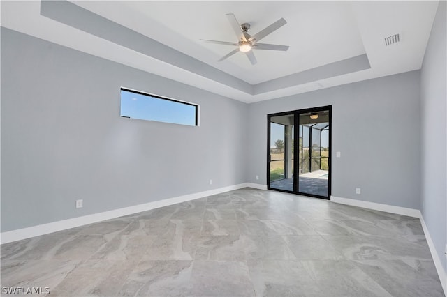 tiled empty room with ceiling fan and a tray ceiling