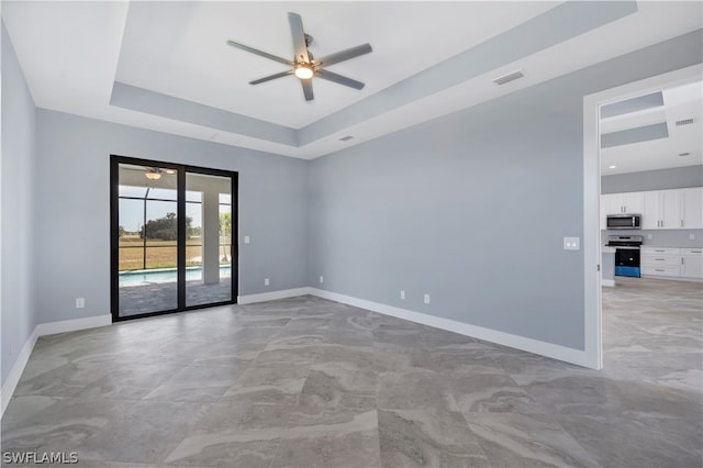 tiled empty room with ceiling fan and a raised ceiling