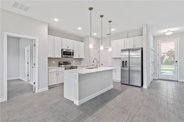 kitchen with a kitchen island with sink, hanging light fixtures, stainless steel appliances, white cabinetry, and light wood-type flooring