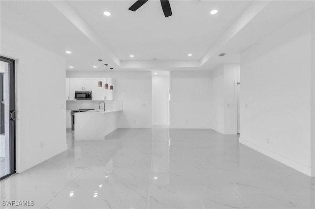 unfurnished room with a raised ceiling, ceiling fan, and sink