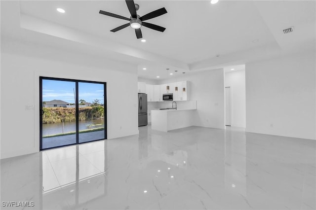 unfurnished living room featuring a raised ceiling, ceiling fan, and sink