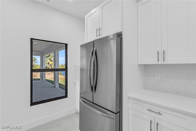 kitchen with white cabinets, stainless steel fridge, light stone counters, and tasteful backsplash