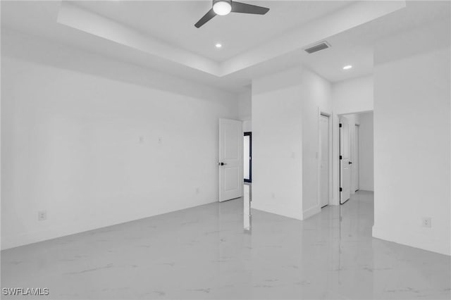 empty room with ceiling fan and a raised ceiling