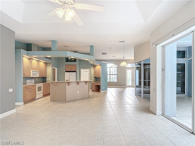 interior space featuring light tile patterned flooring, ceiling fan, white appliances, a center island, and a breakfast bar area