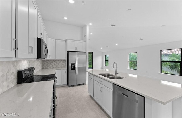 kitchen with light stone counters, stainless steel appliances, white cabinetry, and sink