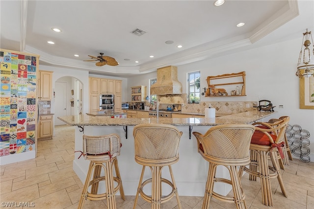 kitchen featuring custom exhaust hood, backsplash, a kitchen bar, light tile floors, and a raised ceiling