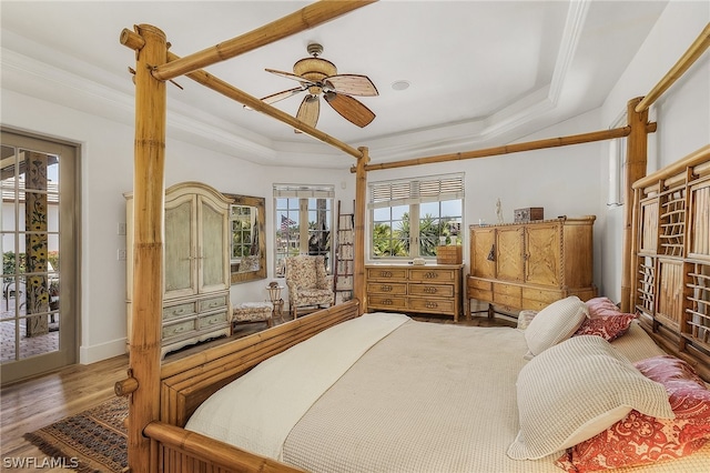 bedroom with ceiling fan, a tray ceiling, access to outside, ornamental molding, and hardwood / wood-style flooring